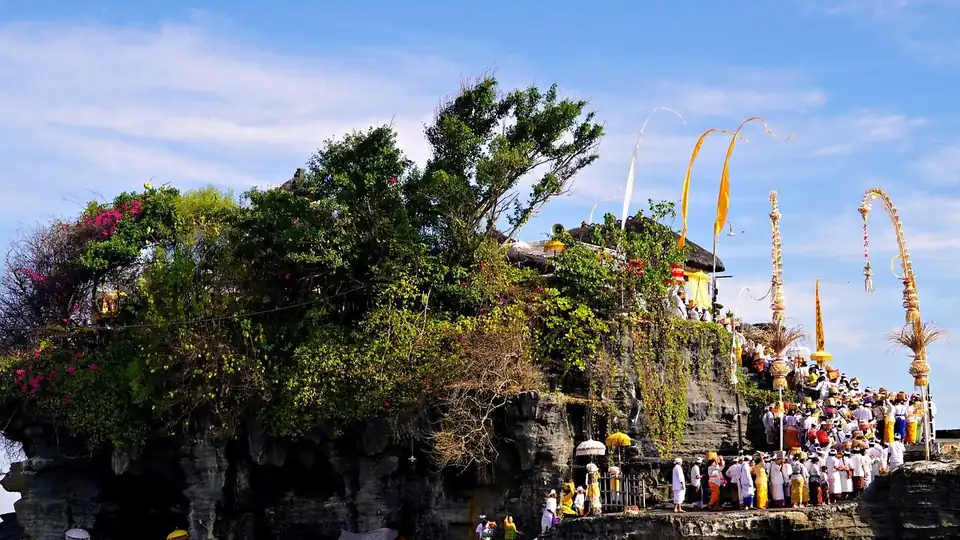 Worshippers in ceremonial white carrying offerings up the rock, penjor poles along the path