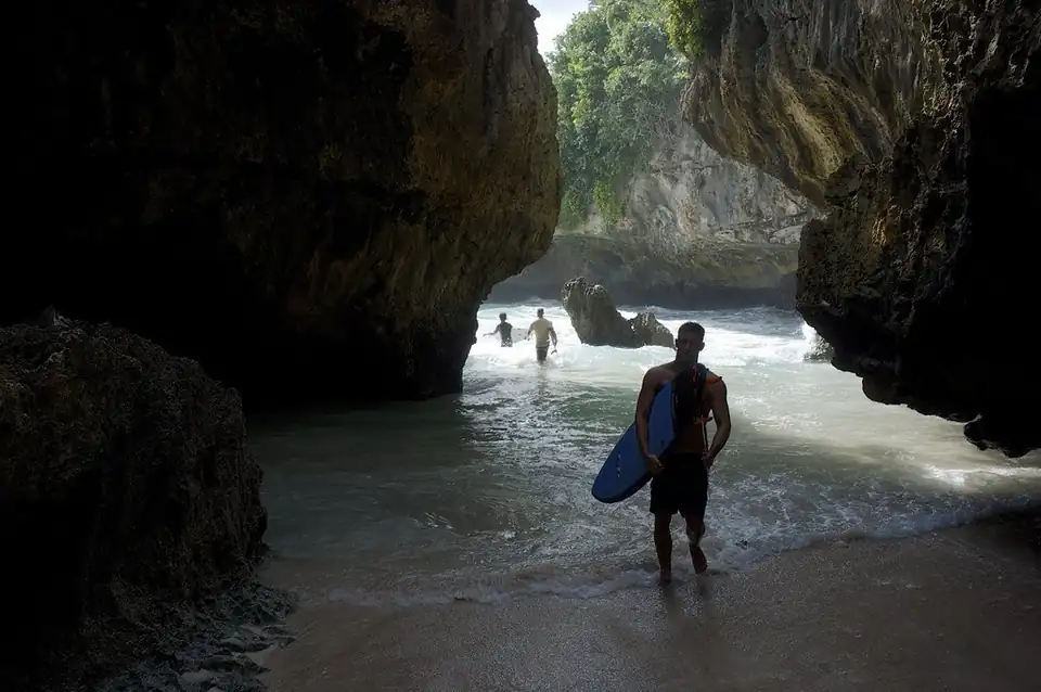 A surfer walking out through the cave at Suluban