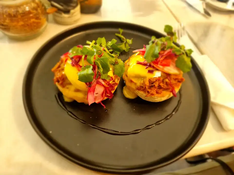 Eggs benedict with pulled pork and pickled vegetables on a black plate at a Bali cafe