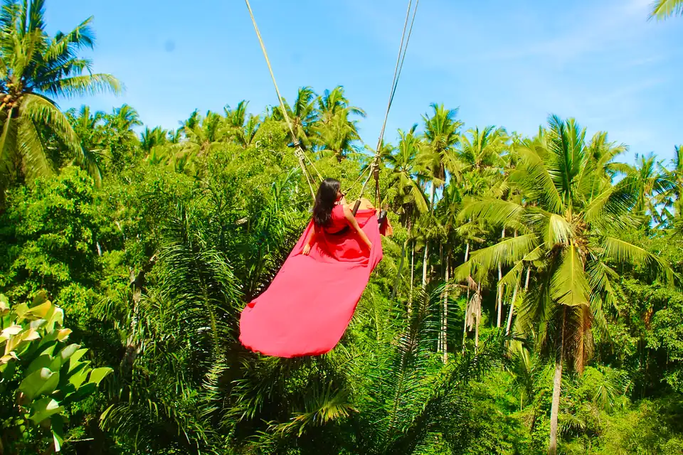 A swing rider in a long red dress above the palms