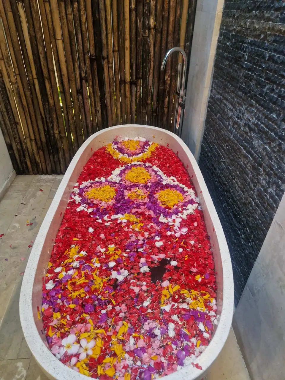 A stone bath filled with red, purple and yellow flower petals arranged in patterns on the water
