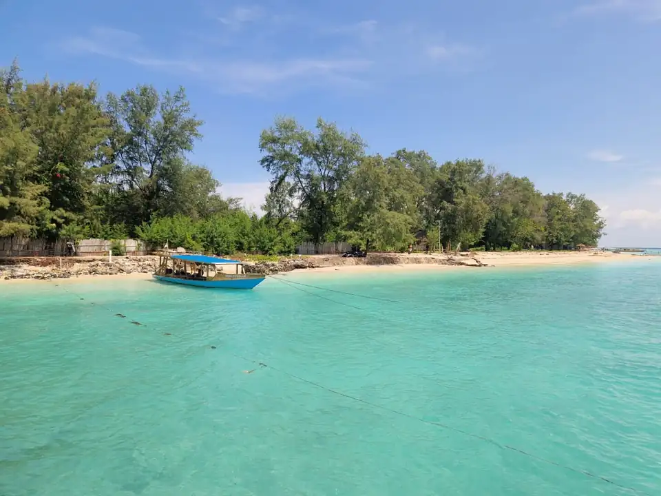 A local boat moored off a white-sand beach backed by casuarina trees on the Gili Islands