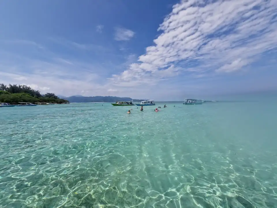 Snorkellers in water clear enough to read the sand ripples below them
