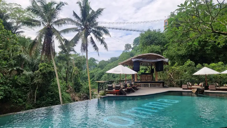 An infinity pool built out over a jungle valley, with a footbridge strung across behind