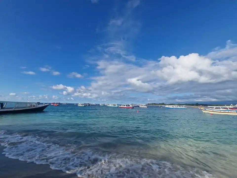 Speedboats and outriggers moored in shallow water off a Bali beach under a bright sky