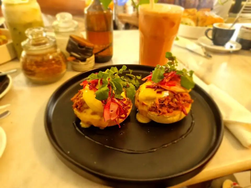 Eggs benedict topped with pulled pork and pickled vegetables on a black plate in a Bali cafe