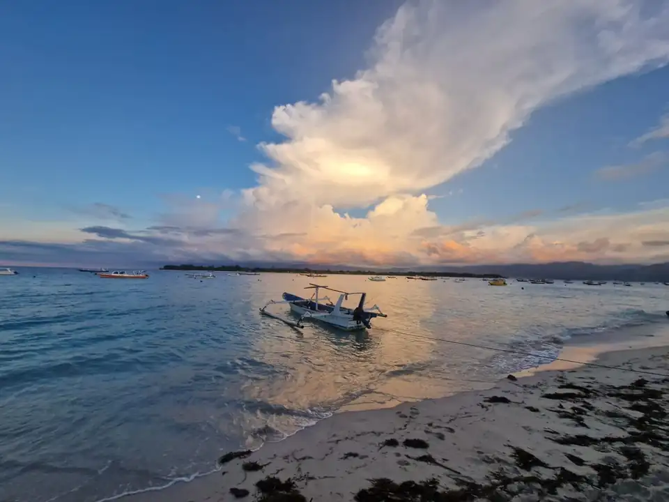 A traditional jukung outrigger at the water's edge as the sun sets behind a distant coastline