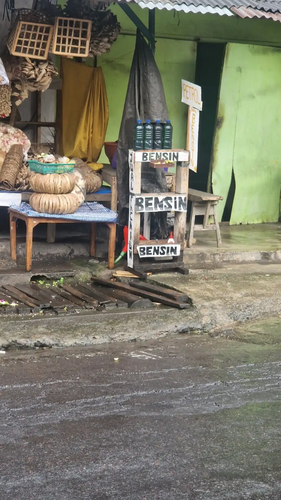 Bottles of petrol labelled bensin for sale on a wooden rack at a roadside stall in Bali