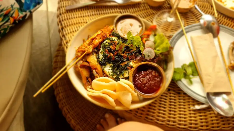 A rice bowl with egg, greens and prawn crackers, served with a pot of sambal on the side