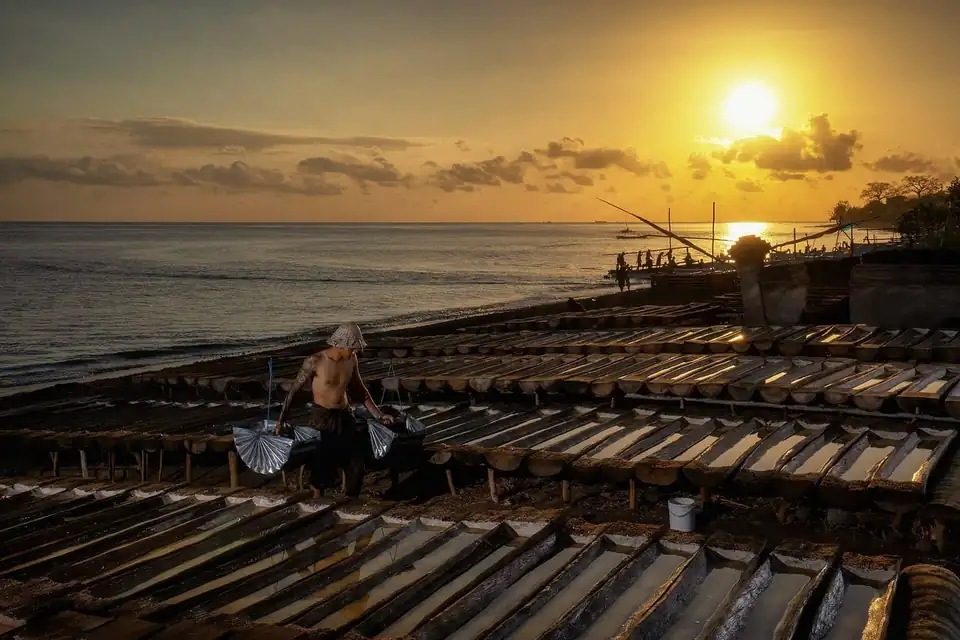 A salt maker working the drying troughs on the shore at Amed