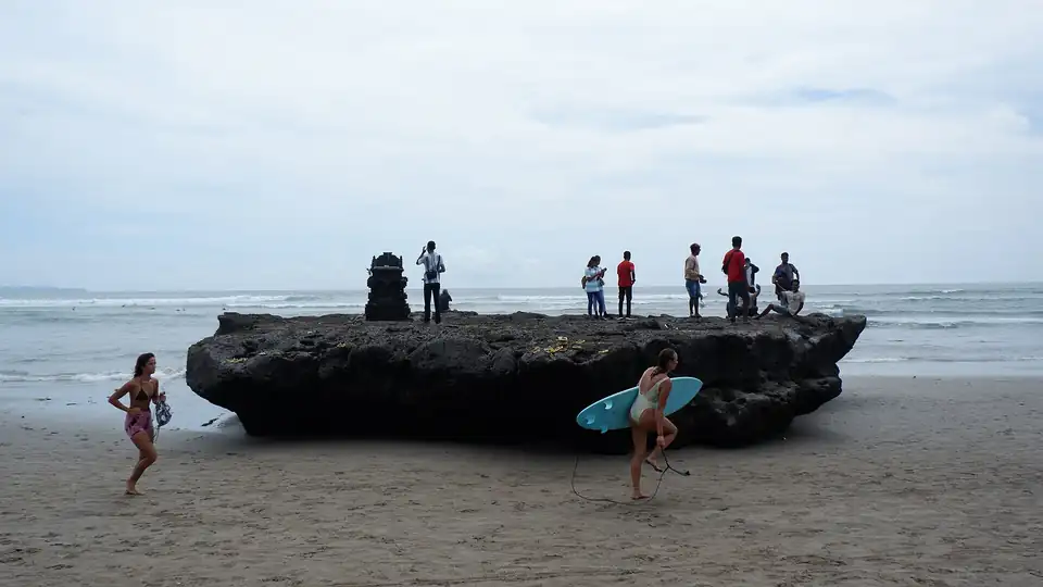 Beachgoers on a dark rock outcrop on the sand at Canggu