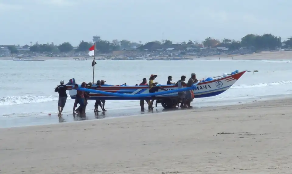 Crew pushing a painted fishing boat off the sand at Jimbaran
