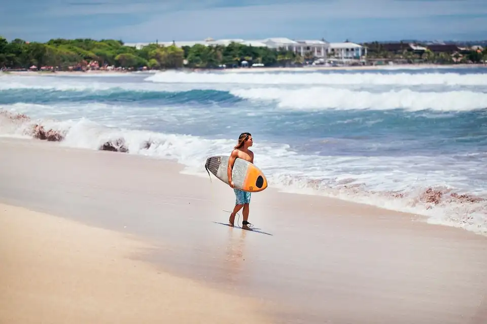 A surfer carrying a board along the sand at Kuta beach